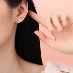 Close-up of letters G and V stainless steel stud earrings worn on the earlobe