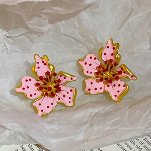 Macro shot of pink enamel flower earrings with red polka dots and matte gold petals