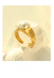 Detail of a minimalist gold wide band ring featuring a white faux pearl on a stone base