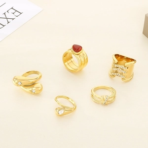 Detailed view of five 18K gold plated rings with rubies and rhinestones on beige surface