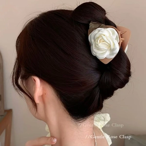 Detail shot of a white fabric camellia hair claw clip styled on the back of a woman's head
