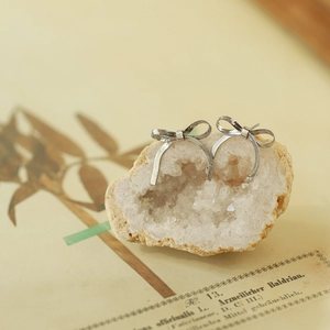 Macro detail of a silver bow earring displayed on white stone with botanical background