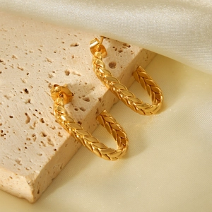 Detailed view of gold C-shaped twisted hoop earrings on beige stone and silk background