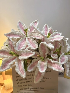 Close-up of handmade crochet lilies in pink and white yarn within a kraft paper bag