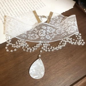 Détail d'un choker en dentelle blanche avec perles multicouches et pendentif poire