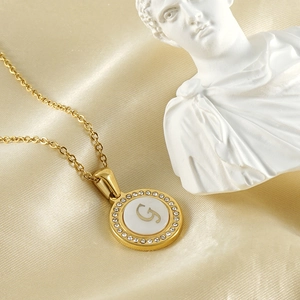 Collier lettre G doré avec nacre et diamants sur fond de soie beige