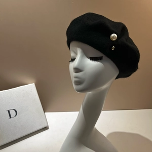 Detail of a black wool beret featuring a large pearl and golden metallic button