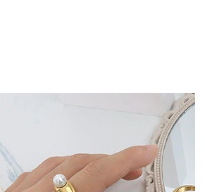 Detail view of a golden fashion ring with a white pearl on a model's finger
