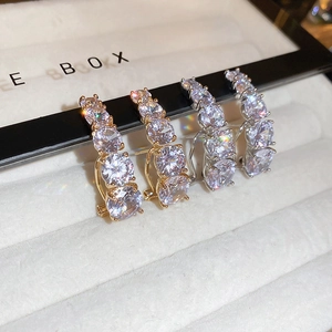 Detail of gold and silver curved stud earrings with four cubic zirconia stones in a row