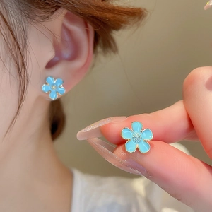Detailed view of light blue floral earrings with gold trim worn on the ear for style