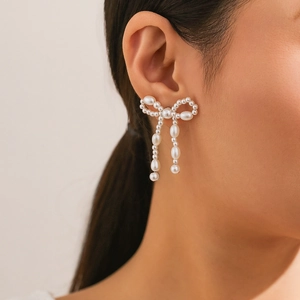 Close-up of model wearing pearl bow stud earrings with dangling drop-shaped pearls