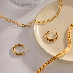 Detail view of gold hammered C-shaped hoop earrings and textured layered necklaces on a ceramic tray