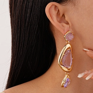 Close-up of gold geometric drop earrings with purple acrylic stones on a female model