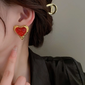 Close-up of red heart earrings with vintage gold textured edges on a model's ear