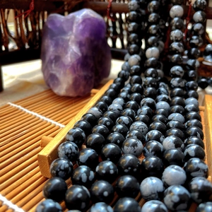 Close-up of round black snowflake stone beads for DIY jewelry on a bamboo tray