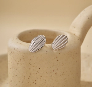 Macro shot of silver shell-patterned earrings on a textured beige ceramic pot edge