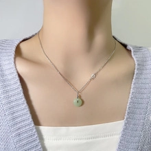Detail of silver chain necklace with light green round donut pendant on model's neck