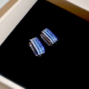 Close-up of triple-layered silver hoop earrings with blue gradient zircons in a gift box