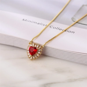 Detailed shot of a gold heart pendant necklace with red gem on a minimalist book background