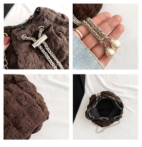 Detail view of brown pleated texture, metal chain strap and pearl beads on bucket bag