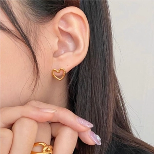 Detailed view of hollow heart stud earrings and matching gold twist ring on model