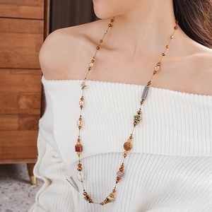 Détail d'un long collier de perles en céramique marron avec breloques papillon et fleurs
