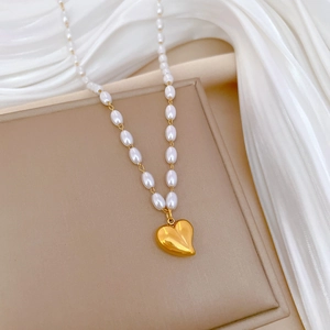 Detailed view of a gold 3D heart pendant on a delicate white pearl necklace chain