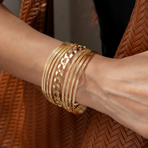 Detail of layered gold geometric bangles and hollow heart link bracelet on wrist