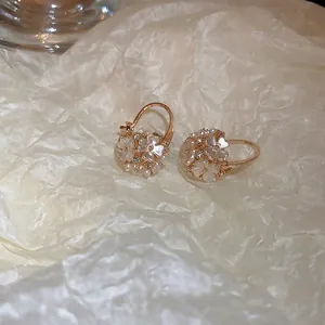 Boucles d'oreilles dorées avec fleurs blanches et zircons sur un fond texturé chaleureux