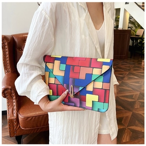Detail view of a colorful geometric clutch bag with a unique gold clasp on a leather sofa