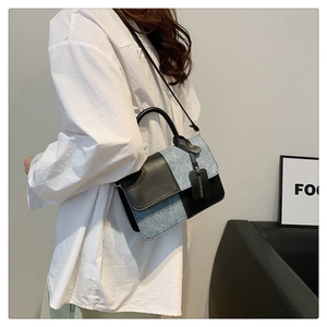 Detail of color-block square bag in black leather and blue denim worn by a model