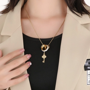 Detail of gold layered key pendant necklace with crystal rings worn on black knitwear
