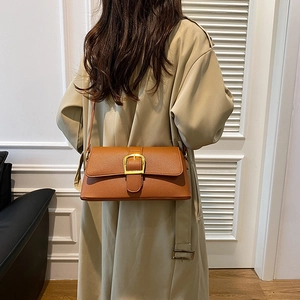 Detailed shot of brown textured leather crossbody bag with elegant gold buckle on a model