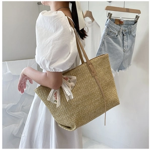 Detail of straw tote bag featuring white lace bow and delicate floral embroidery