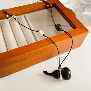 Detail of a black gourd pendant necklace with silver and white beads on a wooden box