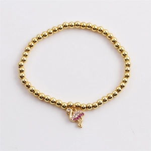 Détail macro du bracelet perlé en or avec pendentifs flamant rose et palmier en zircon