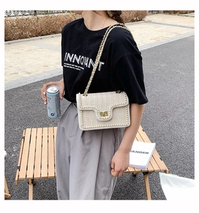 Close-up of woven crossbody bag with pearl trim and golden chain strap in outdoor setting
