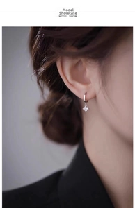 Detail of silver clover earrings with zircon pendant worn by a model in a close-up shot