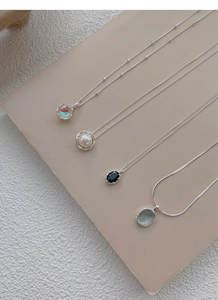Macro shot of silver necklaces featuring pearl, black onyx, and green gemstone pendants
