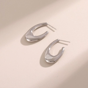 Pair of minimalist silver hollow oval hoop earrings on beige textured background