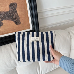 Detailed texture of blue striped cotton linen makeup bag held by hand on white background