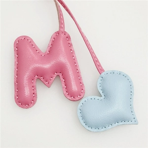 Close-up of handmade leather letter M and blue heart charm with white stitching details