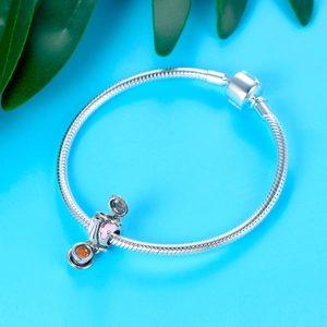 Detail of silver snake chain bracelet featuring a teapot charm with pink enamel accents