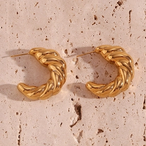 Close-up of golden hollow croissant earrings with twisted texture on beige stone