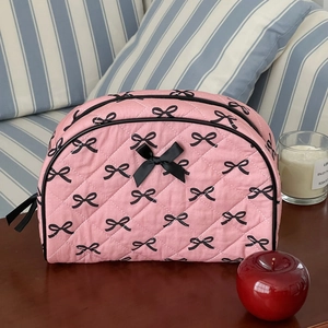 Detailed view of pink quilted makeup bag with black bow patterns on wooden surface