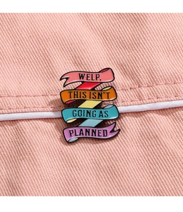 Macro shot of colorful enamel pin with motivational English quote on denim fabric