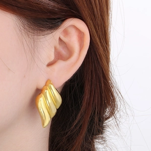 Macro detail of 18K gold-plated wing earrings showing layered wavy texture on model