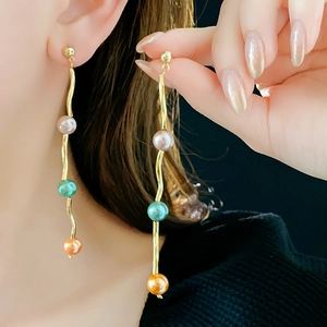Detail of elegant S-shaped gold wave earrings with pink, green, and orange pearls