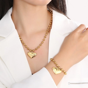 Golden bead chain jewelry set with heart charms worn by model in white suit