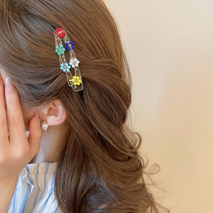 Close-up of colorful beaded floral hair clip with gold chains on brown wavy hair